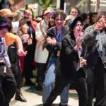 A large group of people dance and laugh together in the gallery