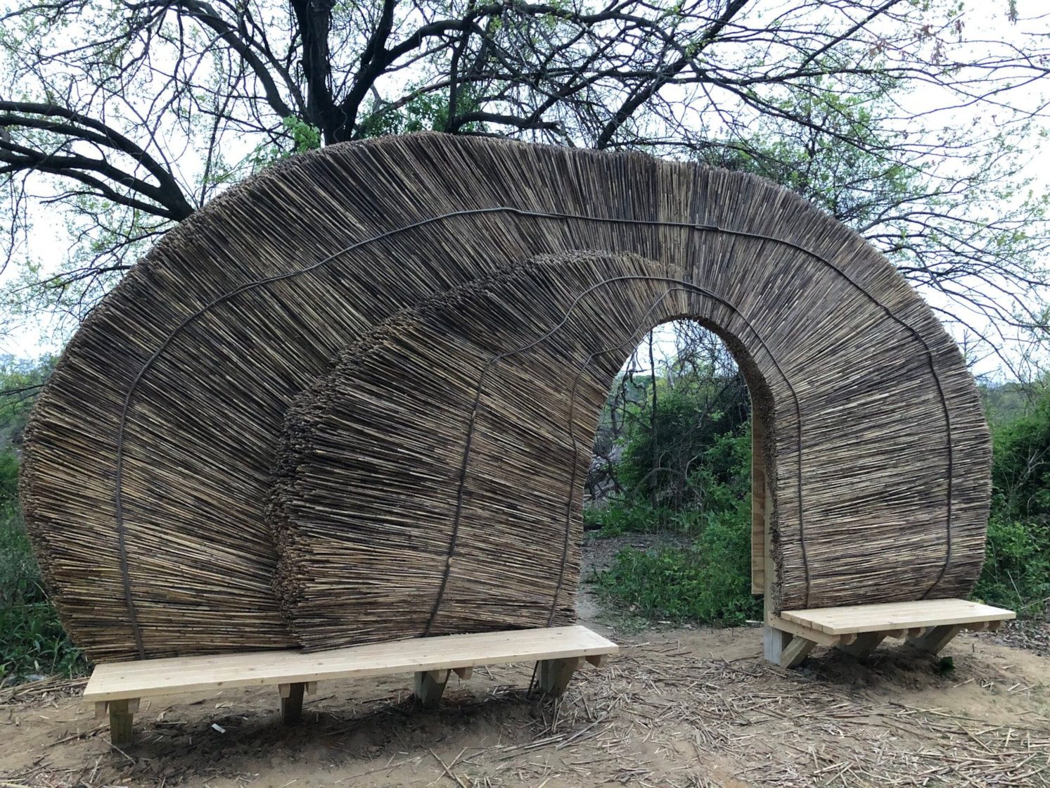 two outdoor benches connected on the back by a straw archway