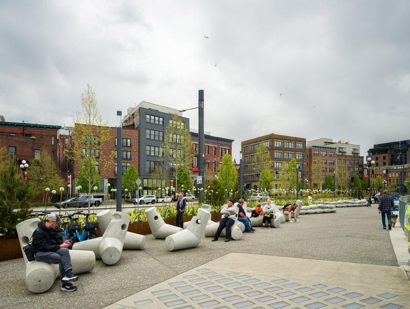 Many cement sculptures sit along a pathway with people sitting on them