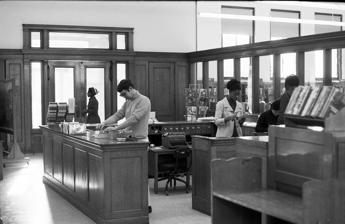 Black and white historic photo of staff at the desk of a library