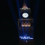 The King Street Station clock tower at night with projected text that reads "I turn my mind away from the winter"