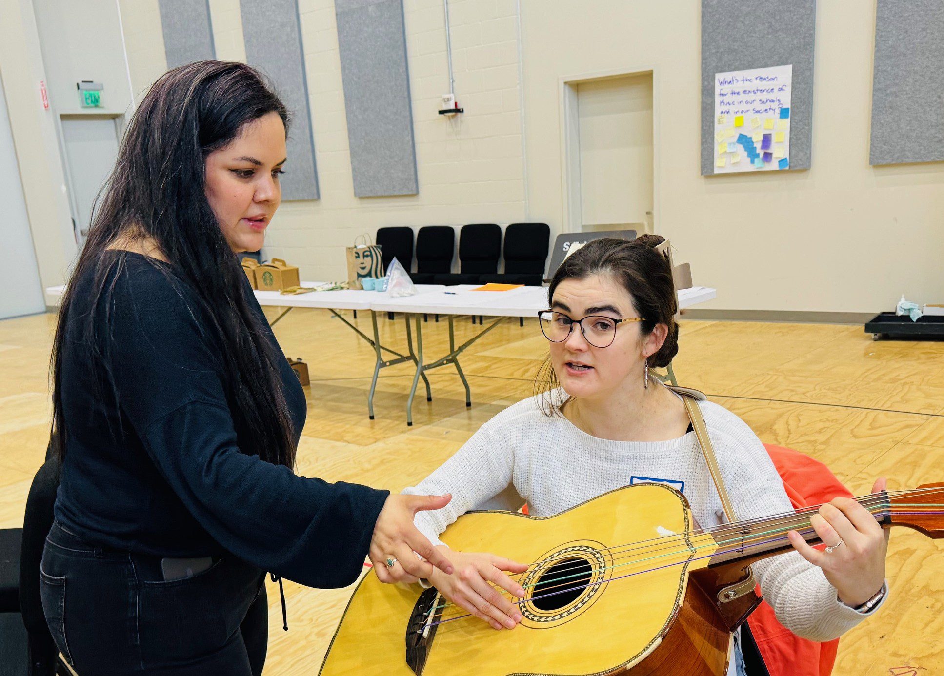 a woman teaches another how to play guitar