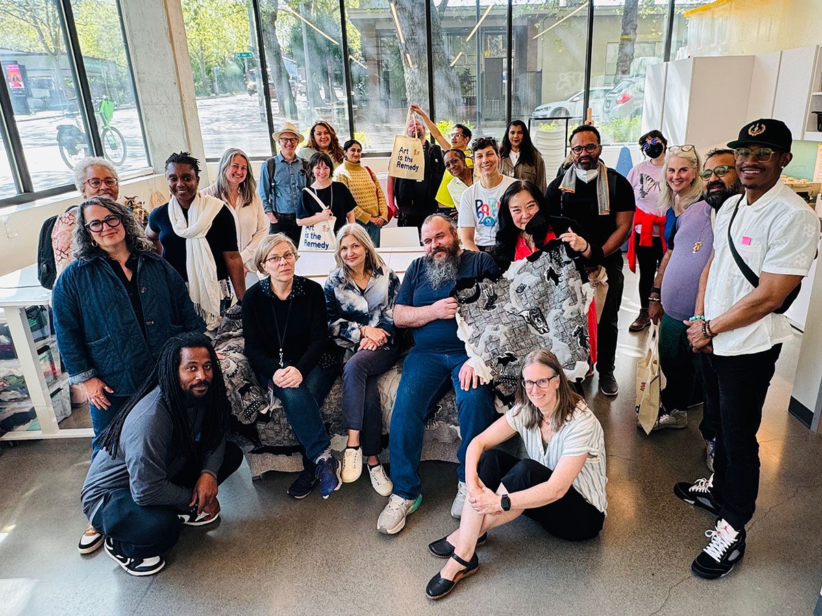 Group photo in a bright studio space. Gülgün is seated on an artwork next to Holly, the ED of Path With Art.