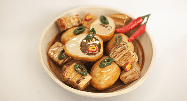 A realistic ceramic sculpture of a bowl of Thit Kho
