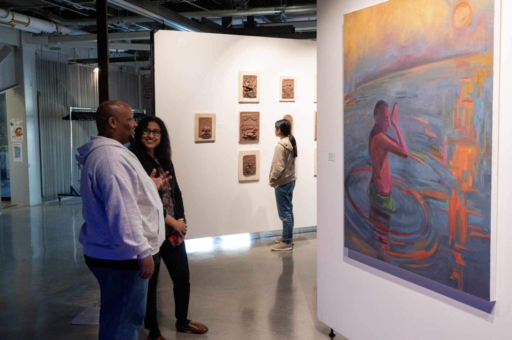 Two people chat in front of a large colorful painting of a figure emerging from the water.