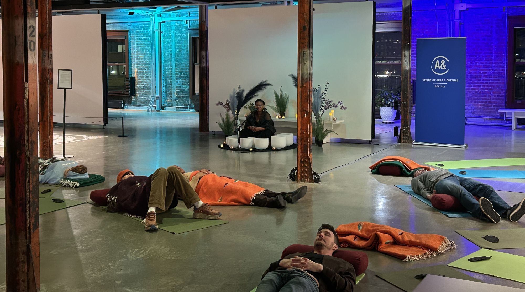 People lay on the gallery floor and listen to a sound bowl performance