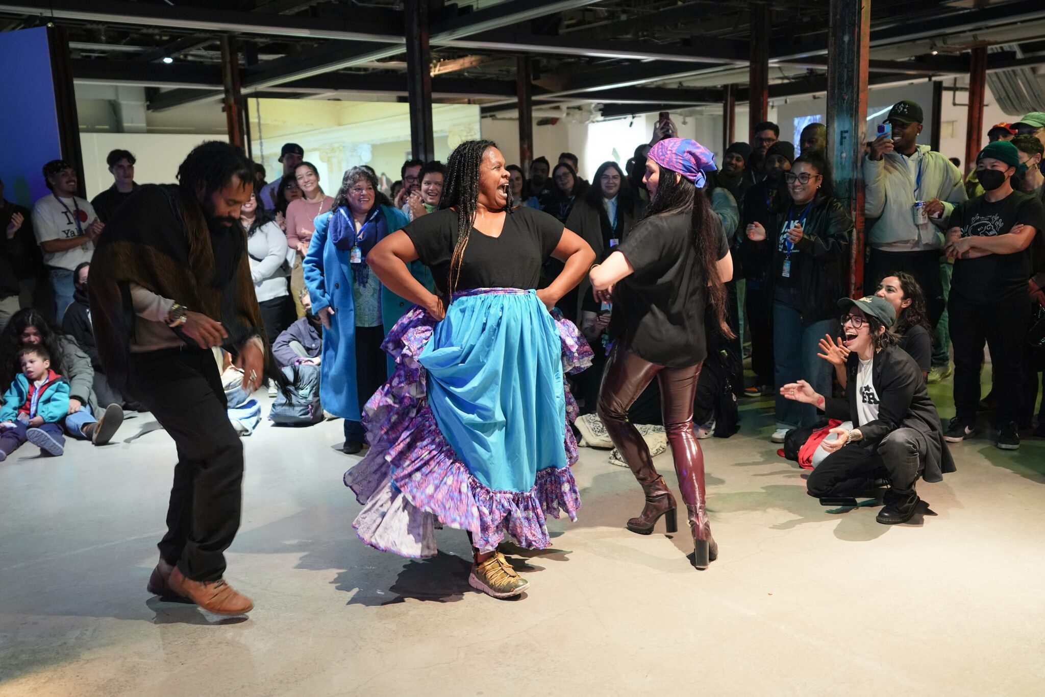 A group of three people dance joyfully to live Bomba as a crowd of onlookers smile and clap.