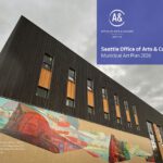 A building façade with wood paneling and a large colorful glass mosaic mural featuring images of a firefighter’s helmet, fire engines, and color-blocked abstract urban and natural features.