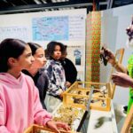 An elder Black man shows historical artifacts to a group of four 5th grade students in a gallery.