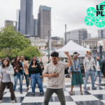 An instructor leads a group in some steps on a dance floor set up on the King Street Station plaza.