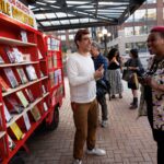 A man talks to people looking at mobile shelves filled with books.
