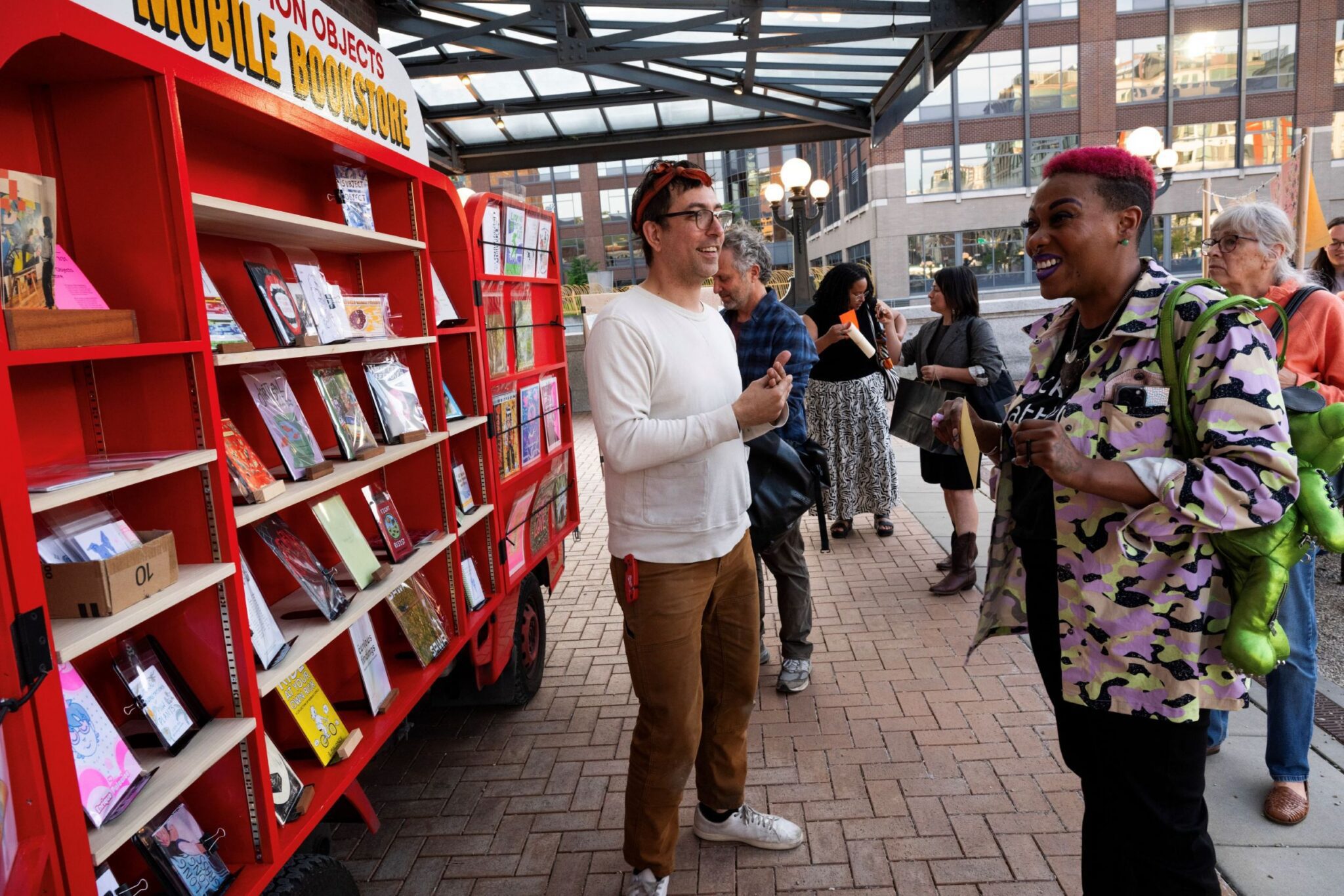 A man talks to people looking at mobile shelves filled with books.