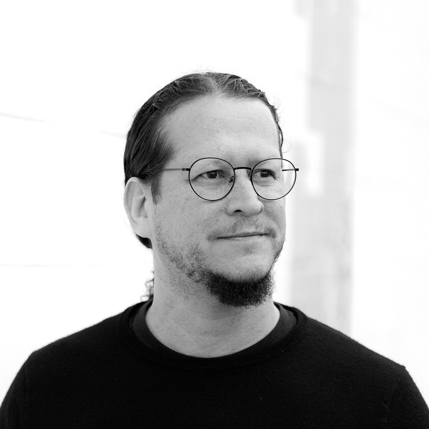 Black and white headshot of a middle aged man with glasses and a small beard looking off to the side