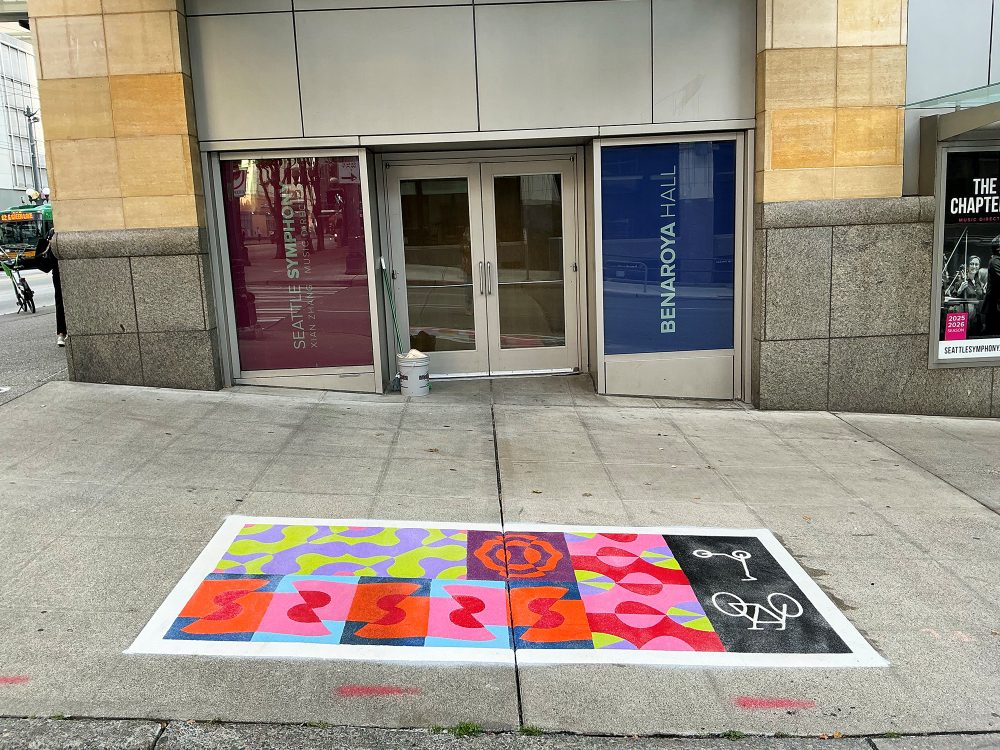 A colorful pattern painted in a rectangle on the sidewalk in front of a Benaroya Hall door.