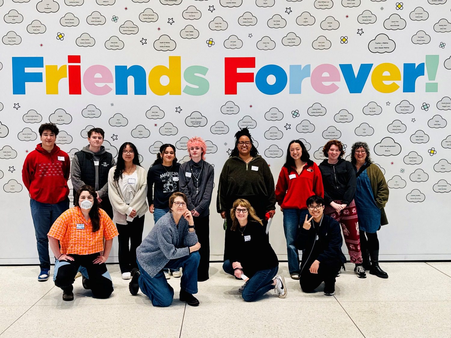 A large group of teenagers posed together under a wall that has colorful lettering reading 