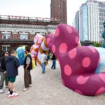 On the plaza of King Street Station sits a large colorful sculpture with an archway. People chat around it and walk through the arch.