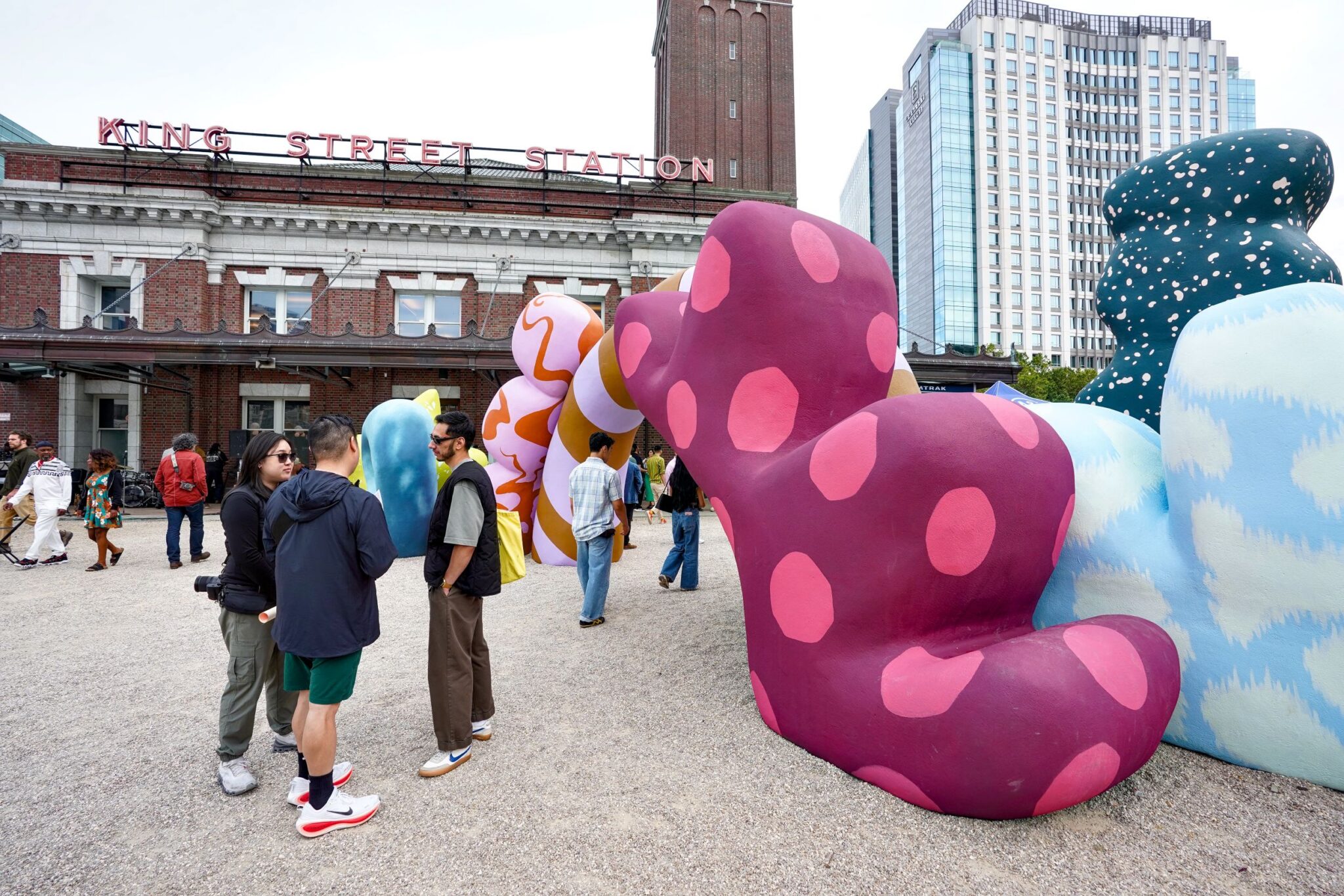 On the plaza of King Street Station sits a large colorful sculpture with an archway. People chat around it and walk through the arch.