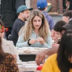 People sit at tables full of art supplies.