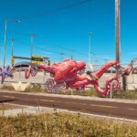 An artwork of a giant red octopus sprawls across a metal chain fence