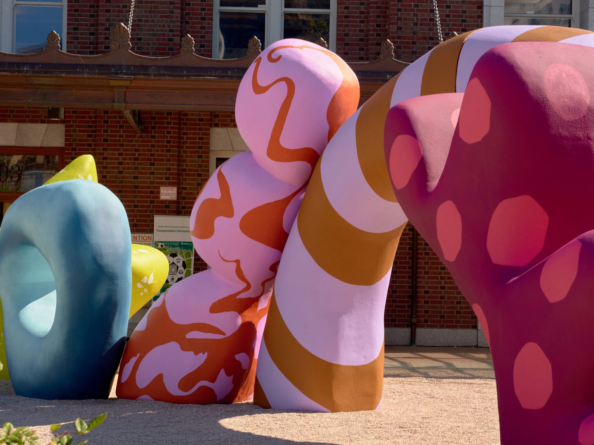 Side view image of Alex Proba's Clouds of Belonging. Five of abstract shapes (shown) are in colors of yellow; teal; pink with orange; rust and purple stripes; and shades of red.