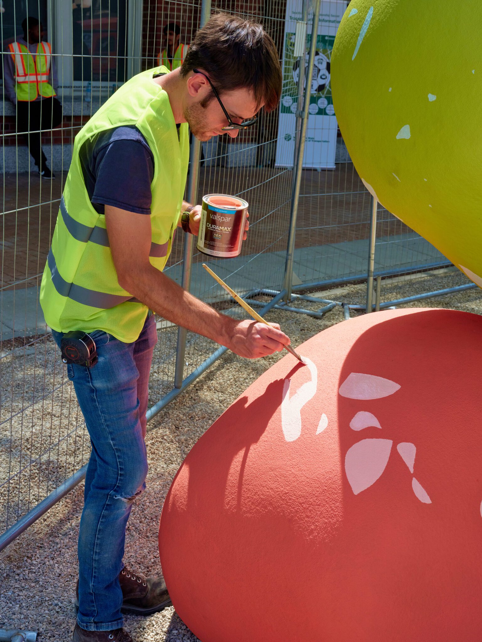 A person painting on one of the red abstract shapes of the installation.