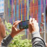 A man holds up a phone displaying a colorful AR simulation.