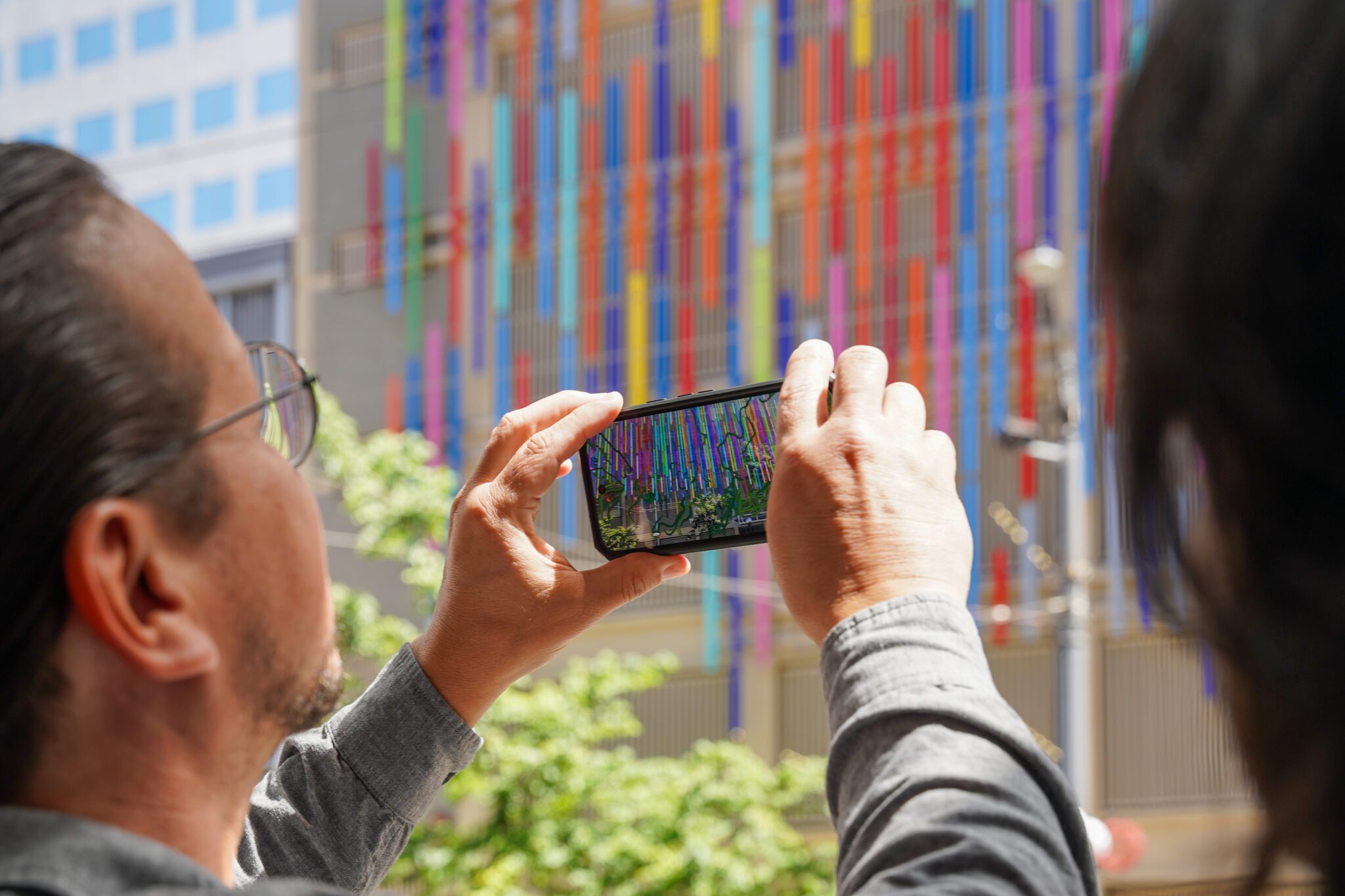 A man holds up a phone displaying a colorful AR simulation.