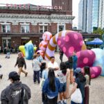 On the plaza of King Street Station sits a large colorful sculpture with an archway. People chat around it and walk through the arch.