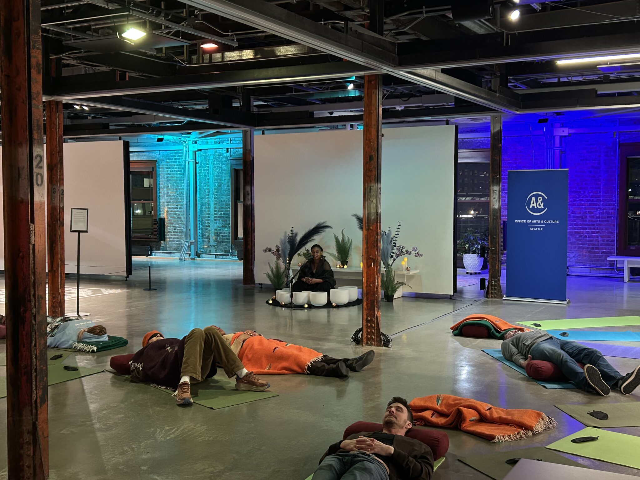 People lie on the floor of ARTS at King Street Station as Stephanie Ann Ball sits with sound bowls.
