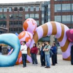 A crowd stands around a large colorful art installation on the King Street Station plaza.