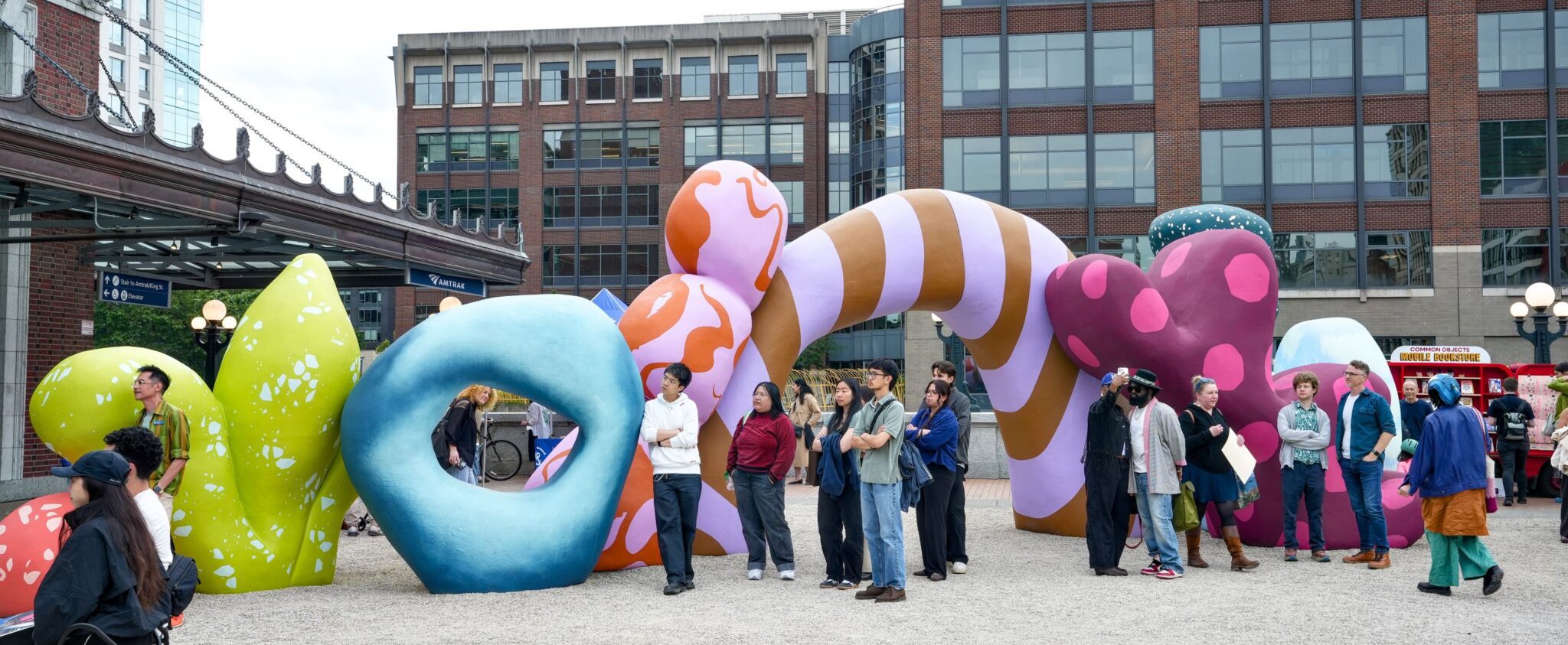 A crowd stands around a large colorful art installation on the King Street Station plaza.