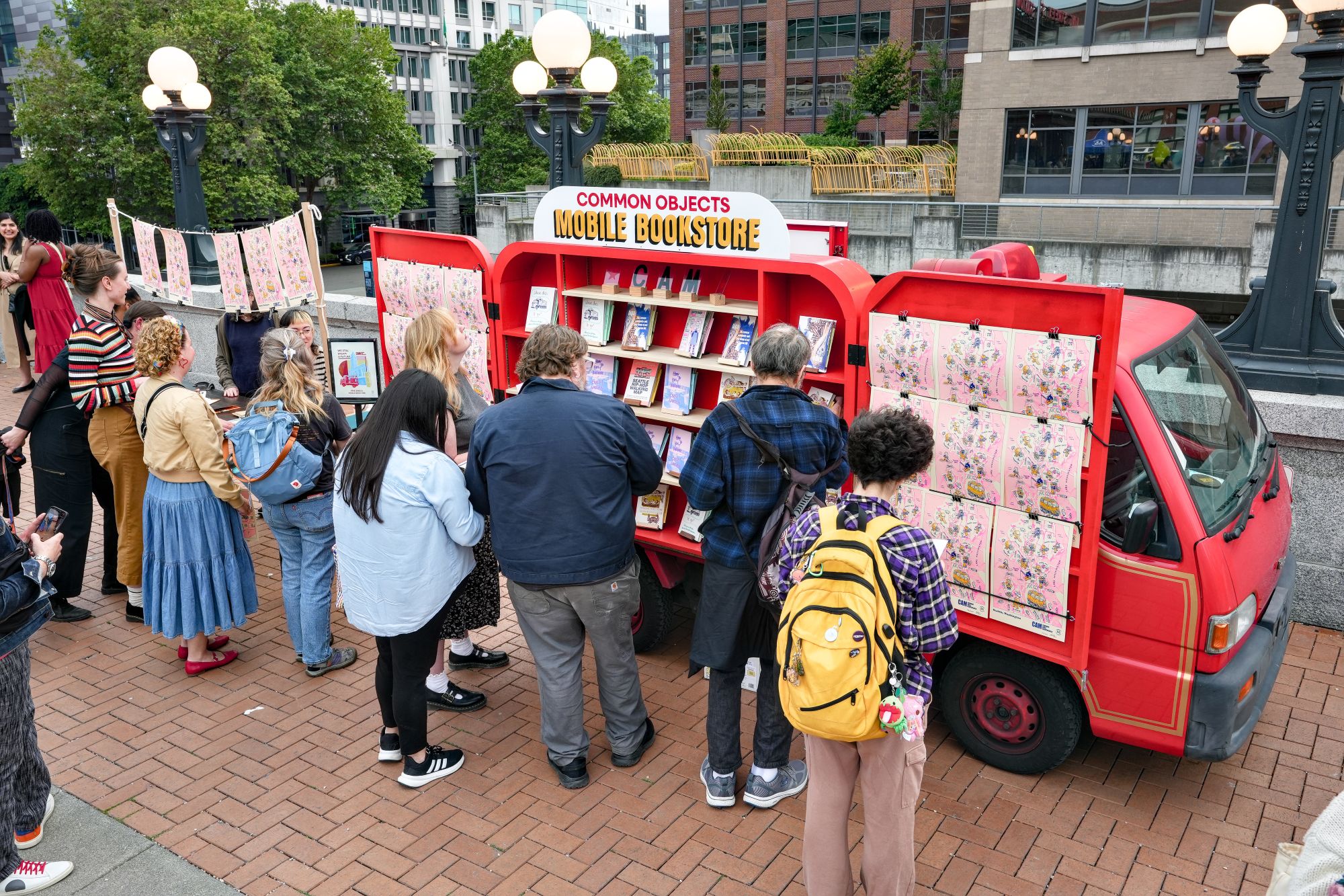 A crowd gathers around an old, decommissioned fire truck converted into a zine library and covered in colorful posters