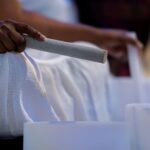 A Black woman's hands holding sound bowl sticks in front of white glass bowls