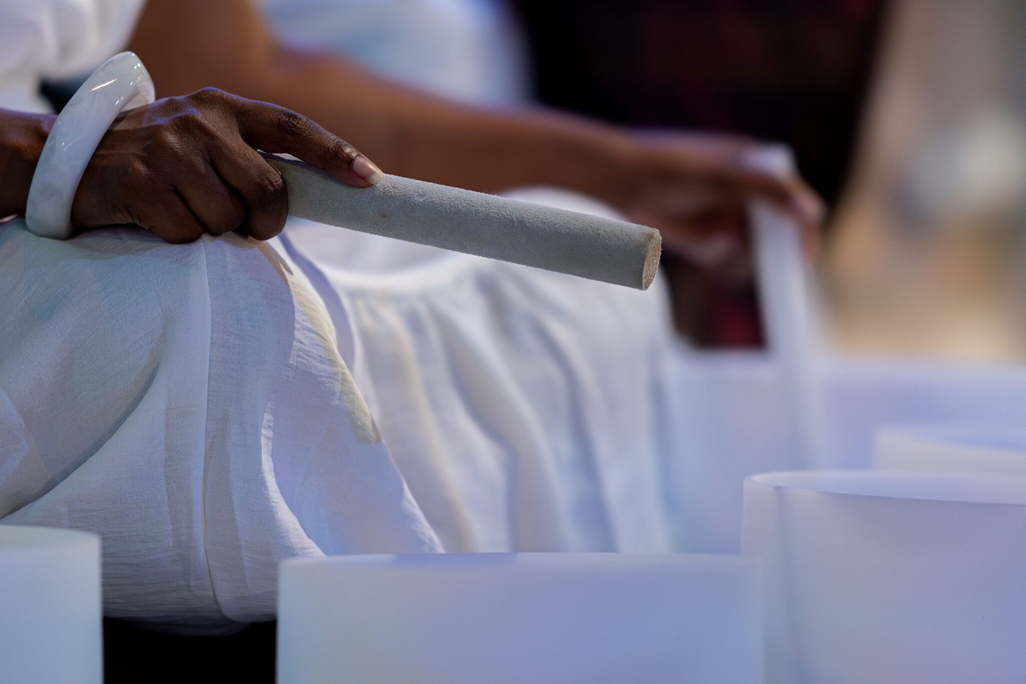 A Black woman's hands holding sound bowl sticks in front of white glass bowls
