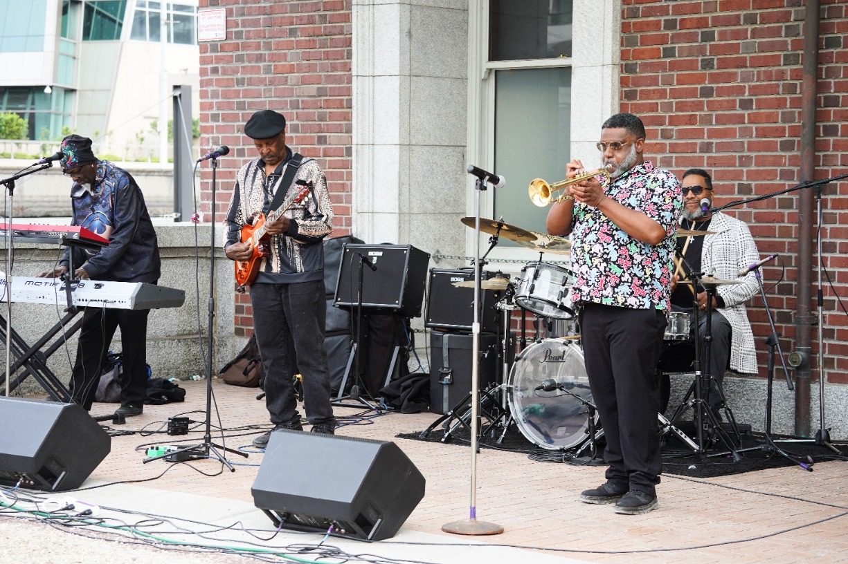 A jazz band of four elder Black musicians play on the King Street Station plaza.