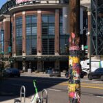 A utility pole covered in bright posters and scraps of paper stands next to a lime bike, in the background you can see T-Mobile Park.