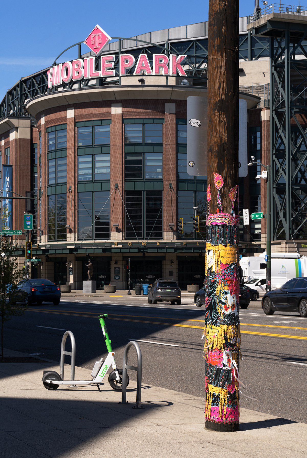 A utility pole covered in bright posters and scraps of paper stands next to a lime bike, in the background you can see T-Mobile Park.
