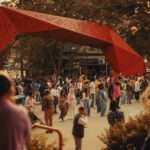 A group of people gather in Hing Hay Park, a large geometric red sculptural form twists over the crowd.